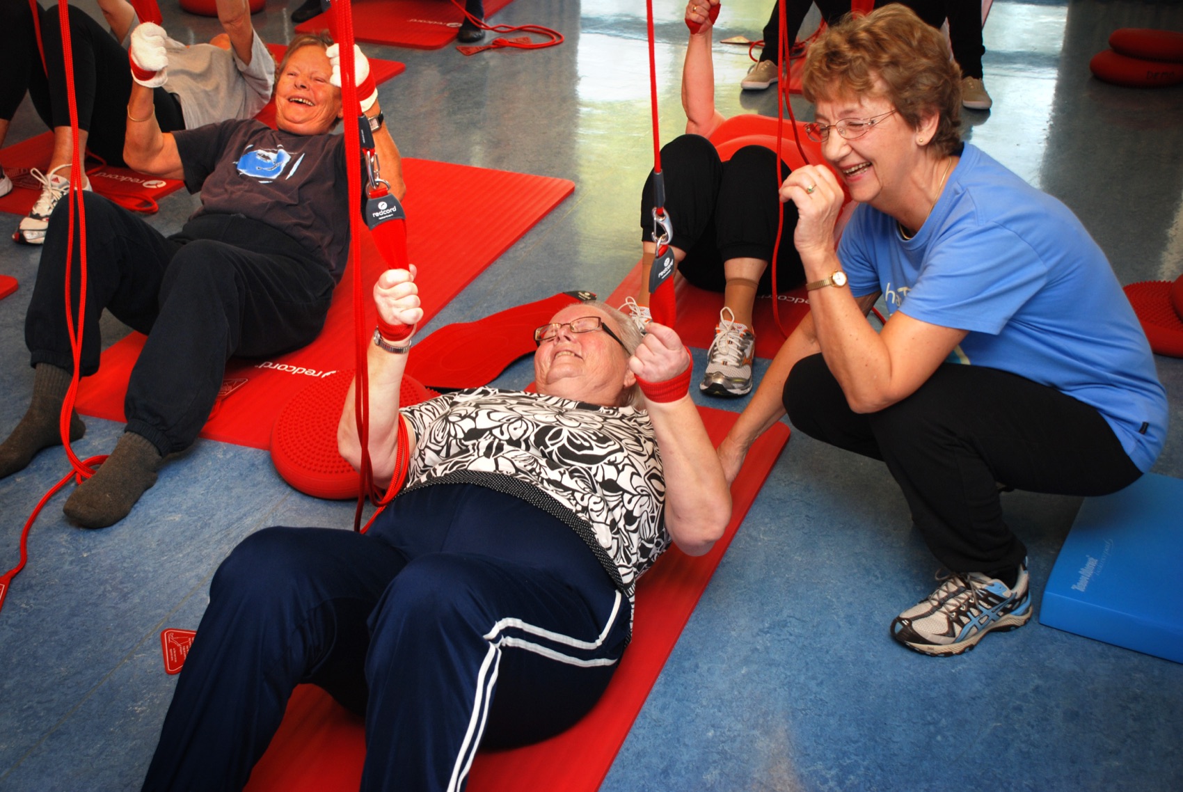 A group training session with an instructor guiding participants on Redcord mats